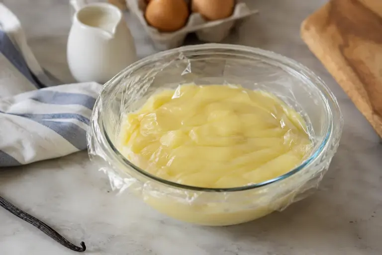 A bowl of smooth vanilla pastry cream with food-safe covering resting directly on the surface.